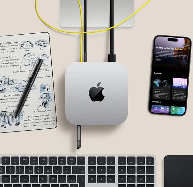 Vue du dessus d’un Mac mini argent sur un bureau avec des câbles et un disque flash branchés dans les ports, avec un clavier sans fil, un pavé tactile, un iPhone et un cahier de notes