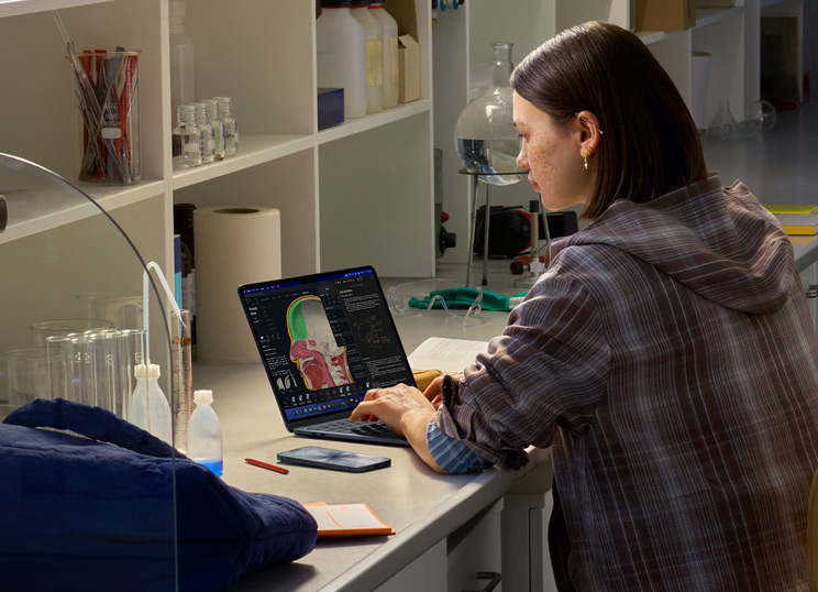 Iemand die in een lab zit en een MacBook gebruikt met meerdere apps op het scherm.