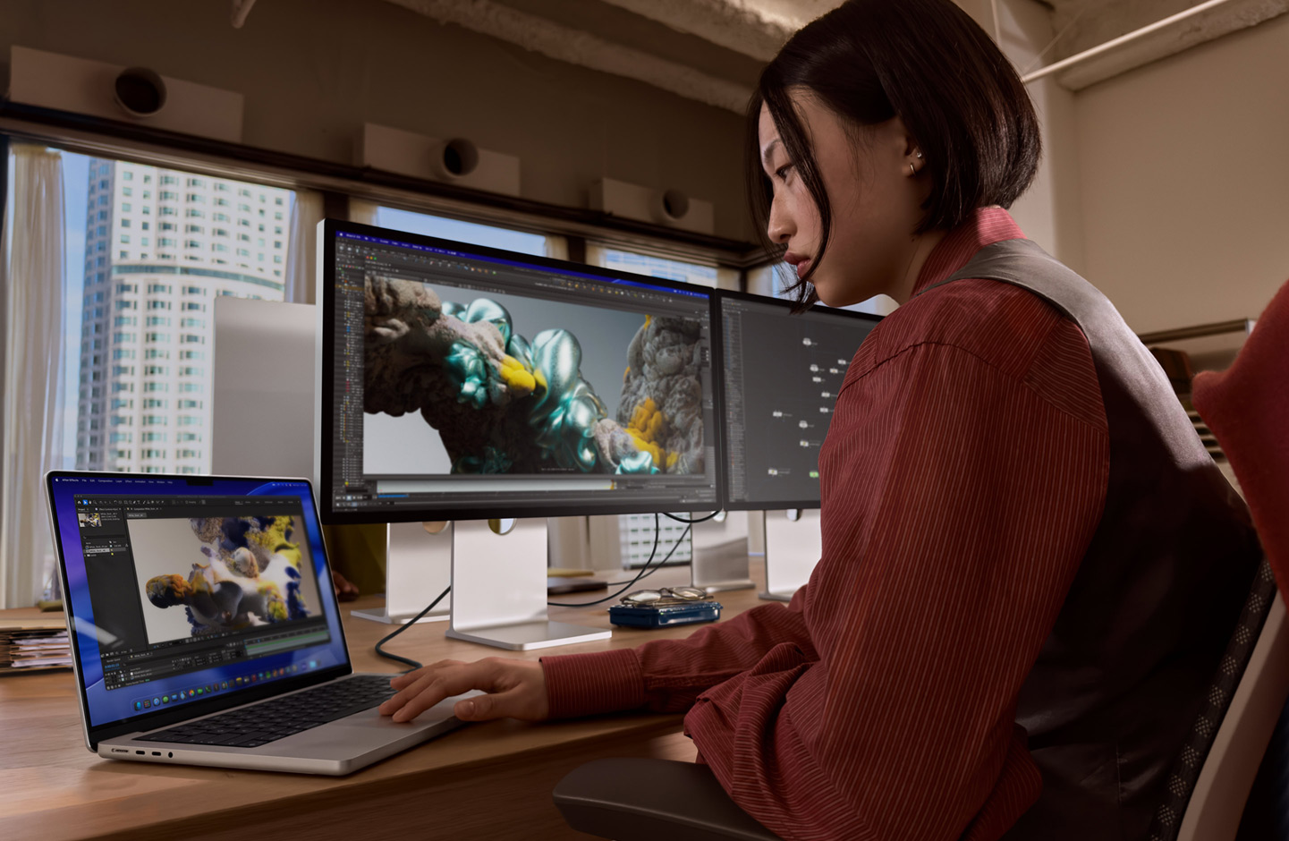 Una persona in un ufficio che lavora su un portatile MacBook collegato a uno Studio Display XDR tramite una porta Thunderbolt 5