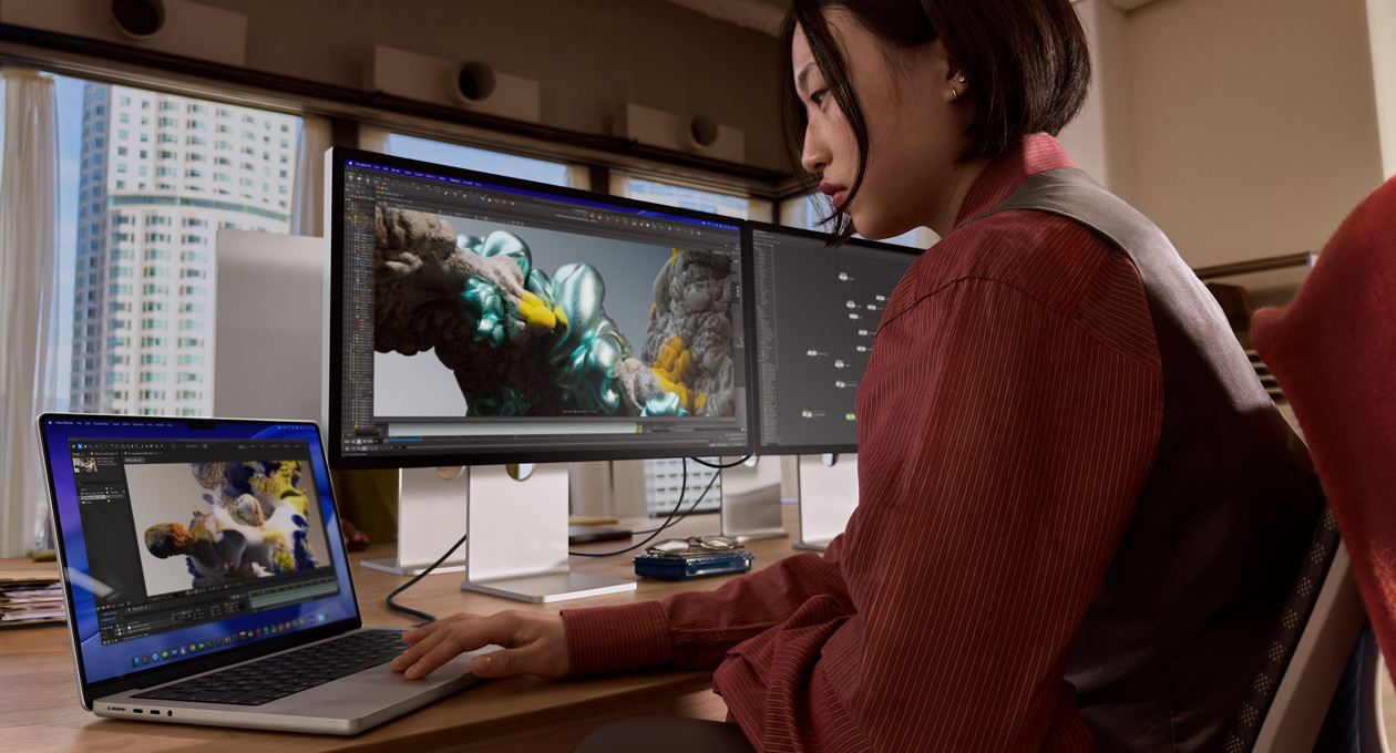 Una persona in un ufficio che lavora su un portatile MacBook collegato a uno Studio Display XDR tramite una porta Thunderbolt 5
