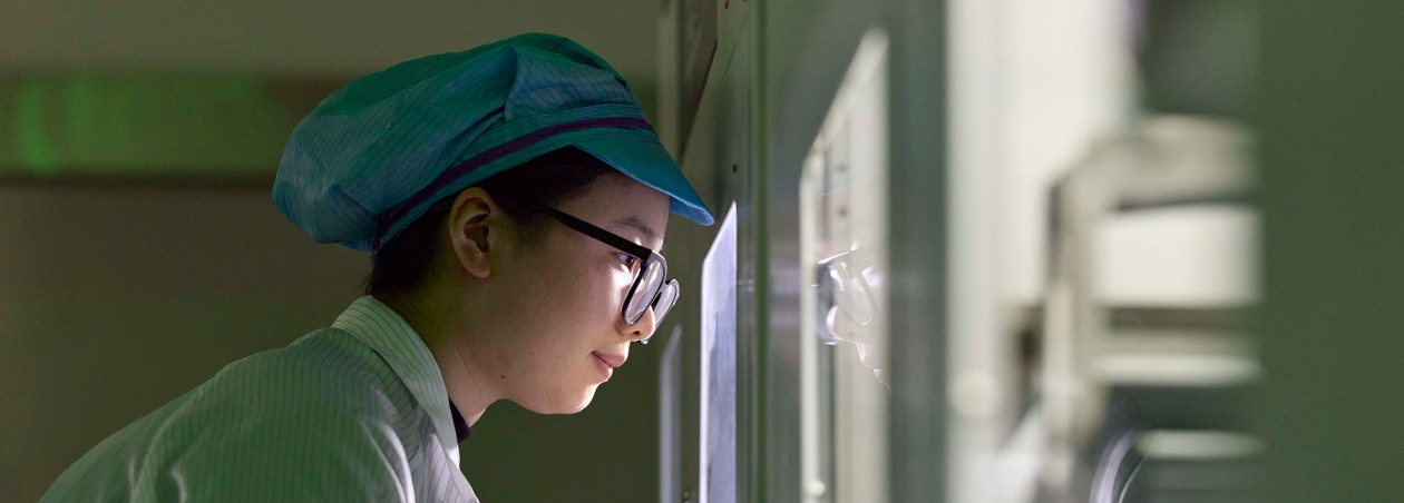 Seorang karyawan yang mengenakan pakaian pelindung dan pelindung mata mengamati perakitan Apple Watch