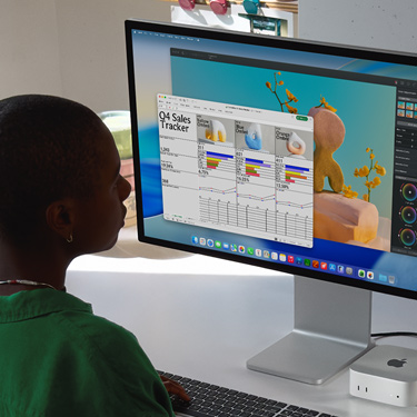 Employee sits and works on an Excel spreadsheet titled 'Q4 Sales Tracker' on iMac and Mac Mini. Behind the Excel spreadsheet is a Pixelmator Pro window and the macOS Tahoe background.