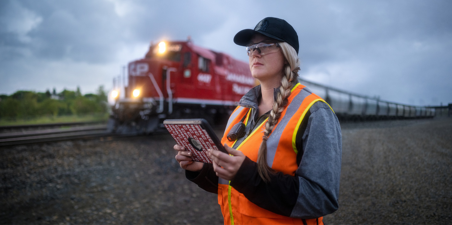 Uma funcionária da ferrovia segura um iPad e observa os trilhos enquanto um trem passa