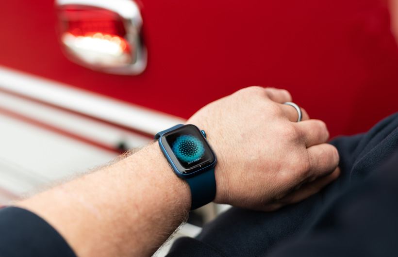 Um braço com o Apple Watch exibe a mensagem Agora inspire, com um caminhão de bombeiros ao fundo