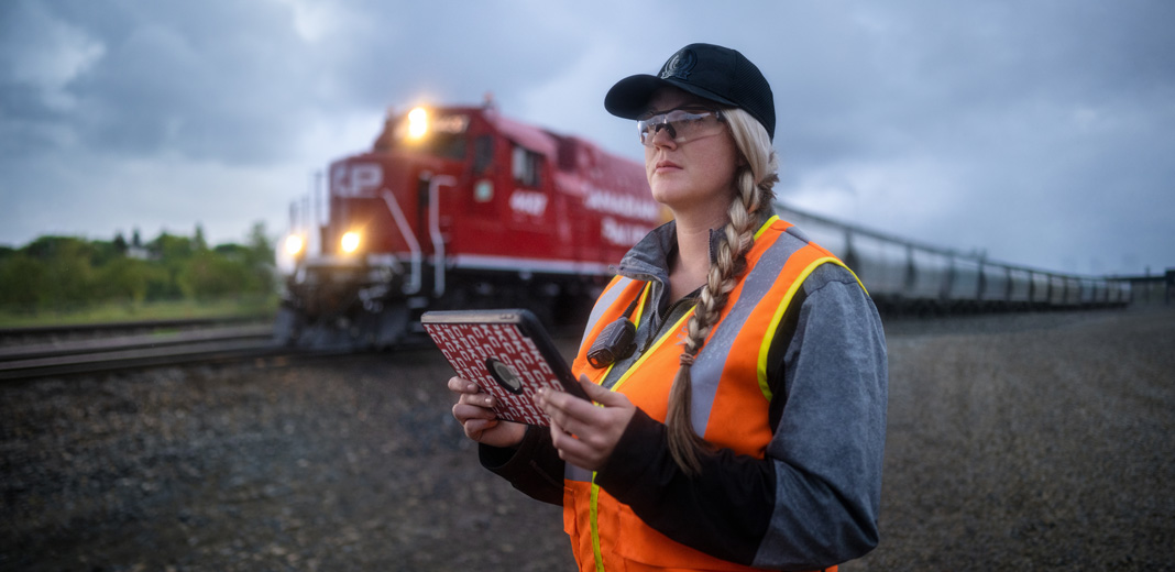 Een spoorwegmedewerker houdt een iPad vast en kijkt uit over het spoor terwijl er een trein voorbij rijdt