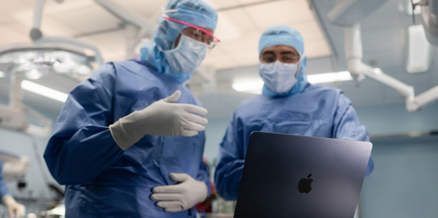 Twee chirurgen in de operatiekamer kijken naar een MacBook, de één gebaart met zijn hand terwijl de ander observeert