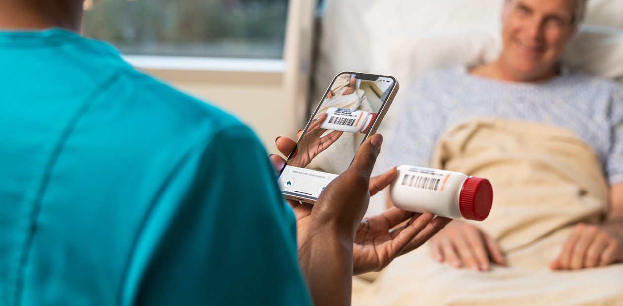 Un membre du personnel infirmier en blouse bleu sarcelle scanne des médicaments à l’aide de son iPhone.