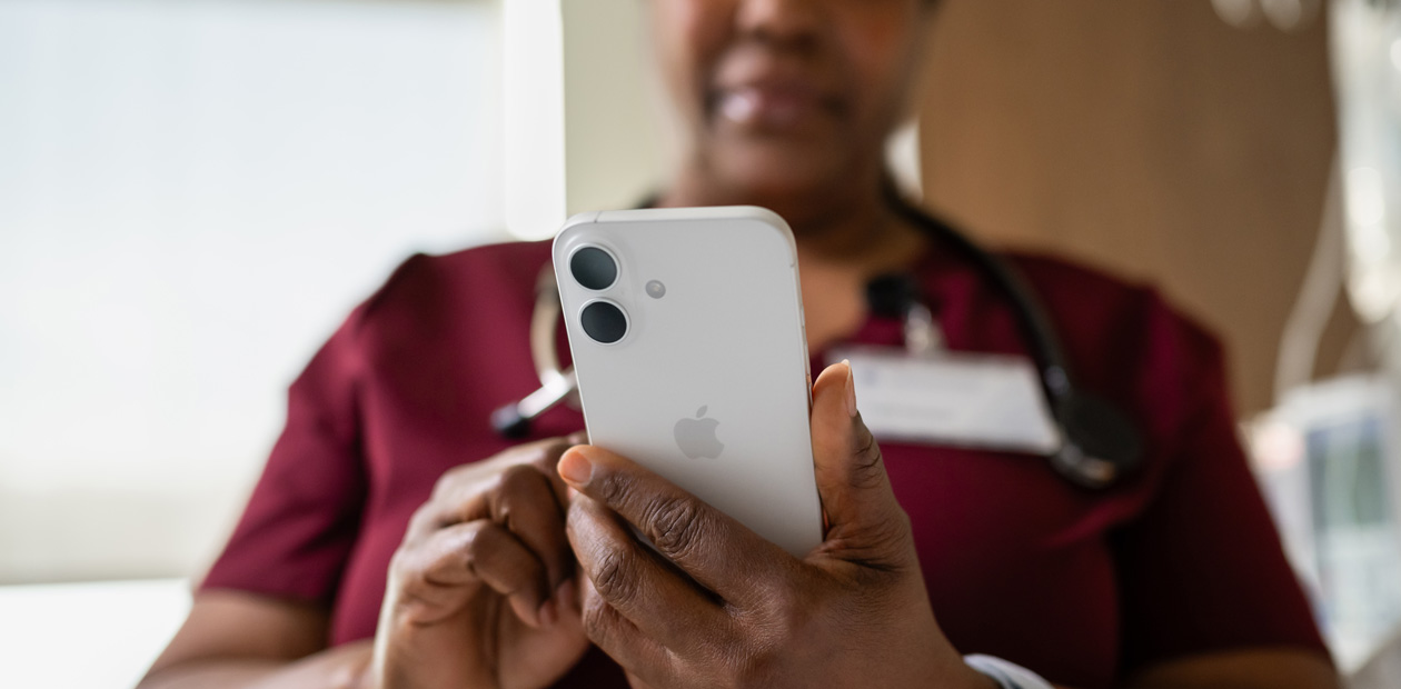 Une infirmière en blouse rouge regarde son iPhone.