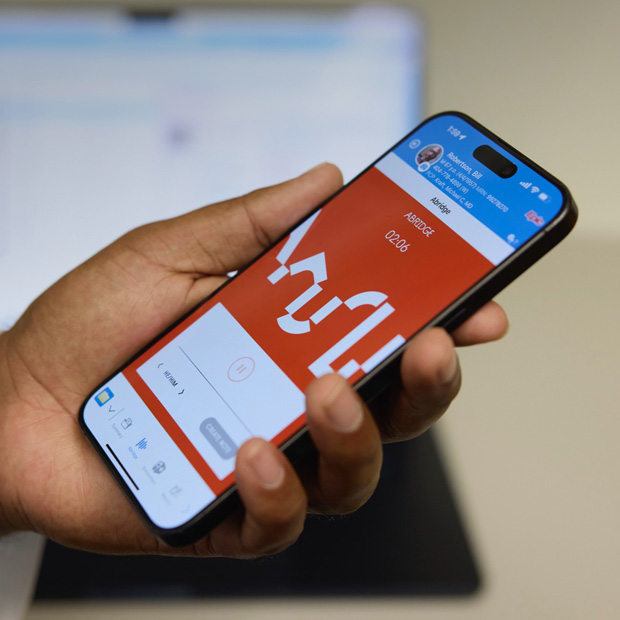Une main tient un iPhone affichant l’app Abridge, qui traduit les conversations entre personnel soignant et patientèle en notes cliniques.