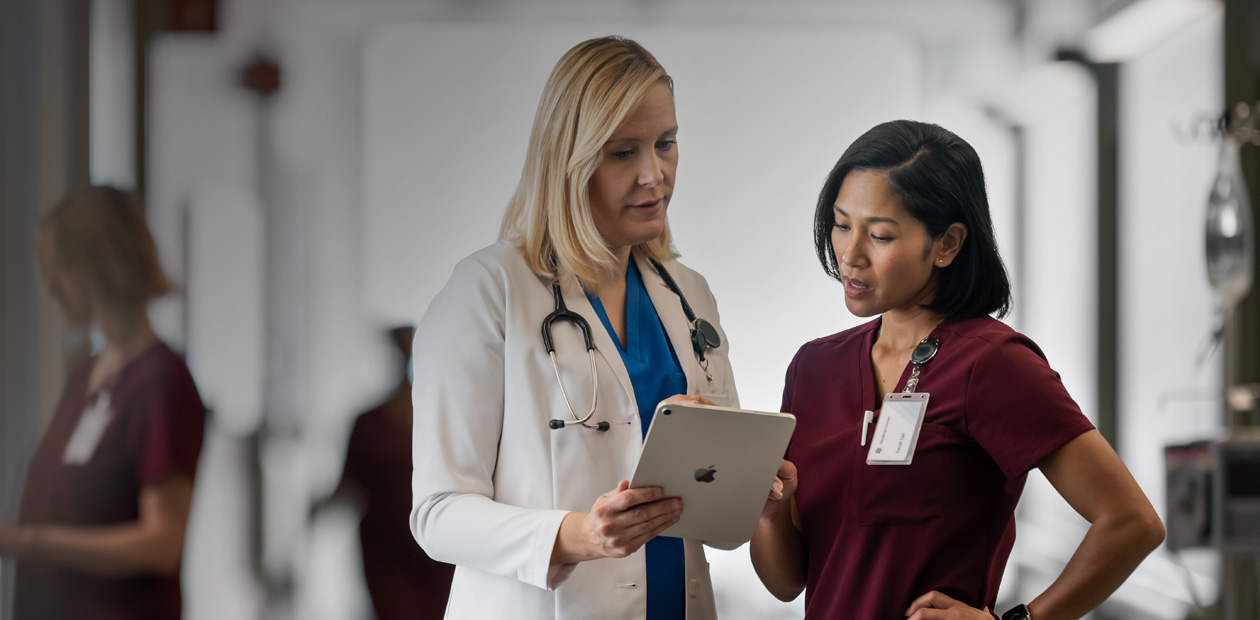 Un médecin et une infirmière consultent ensemble un iPad dans un couloir d’hôpital.