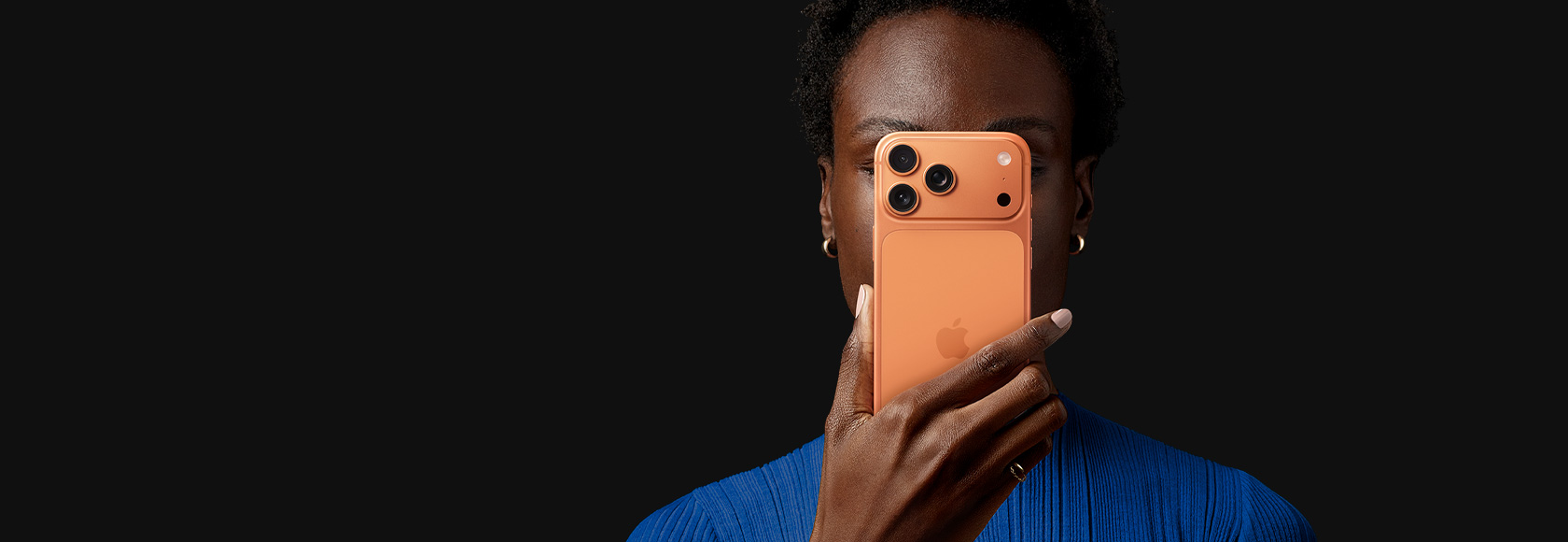 Osoba trzymająca przed twarzą iPhone'a 17 Pro w kolorze kosmicznego pomarańczu z tyłem urządzenia skierowanym na zewnątrz