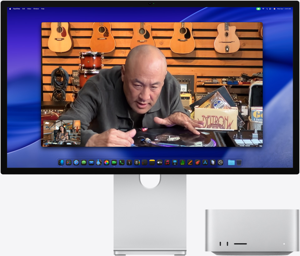 Una persona en una tienda de música mira de cerca un tocadiscos durante una videollamada en un monitor Studio Display XDR con una Mac Studio debajo